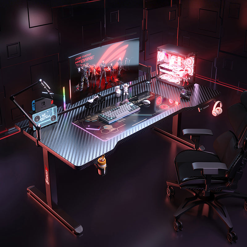 Black K1 Electric Standing Desk with carbon fiber top, RGB gaming setup, and red accent lighting.
