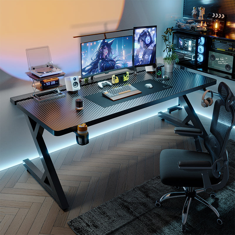 Black gaming desk setup with dual monitors, carbon-fiber surface, and LED backlighting in a modern room.